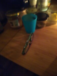 eine unscharfe aufnahme. auf einem tisch liegt eine lesebrille, eine butterdose, ein honigglas und ein kleines glas mit schraubdeckel sind zu sehen.