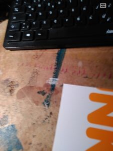 bekritzelter schreibtisch, ein stück tastatur, ein teil einer grafischen postkarte.